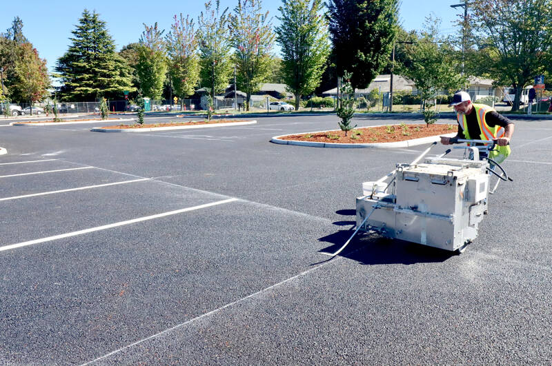 David Gritskie of Stripe Rite from Bremerton guides a stripe painting machine Wednesday east of Port Angeles City Hall. The new parking lot is using permeable pavement over a layer of gravel of 2 feet to 4 feet thick. The project is retrofitting the east city hall parking lot with a new stormwater detention and treatment infrastructure. The project will help manage runoff, slow down peak flow and remove pollutants before connecting and flowing into Peabody Creek. The parking lot will reopen to the public on Monday. (Dave Logan/for Peninsula Daily News)