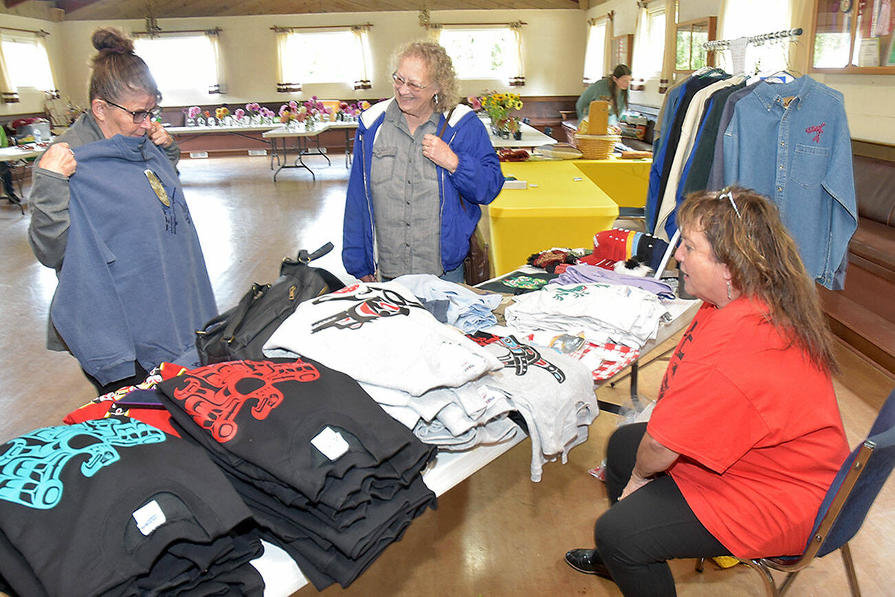 Jackie Leonard of Cottage Grove, Ore., left, examines a sweatshirt while Janet Estes of Joyce looks on at a merchandise table set up by Cindy Kelly at the Joyce Grange Hall on Saturday in Joyce. The venue was one location of the Great Strait Sale, a collection of garage and yard sales by residents along state Highway 112 from Port Angeles to Neah Bay. (Keith Thorpe/Peninsula Daily News)