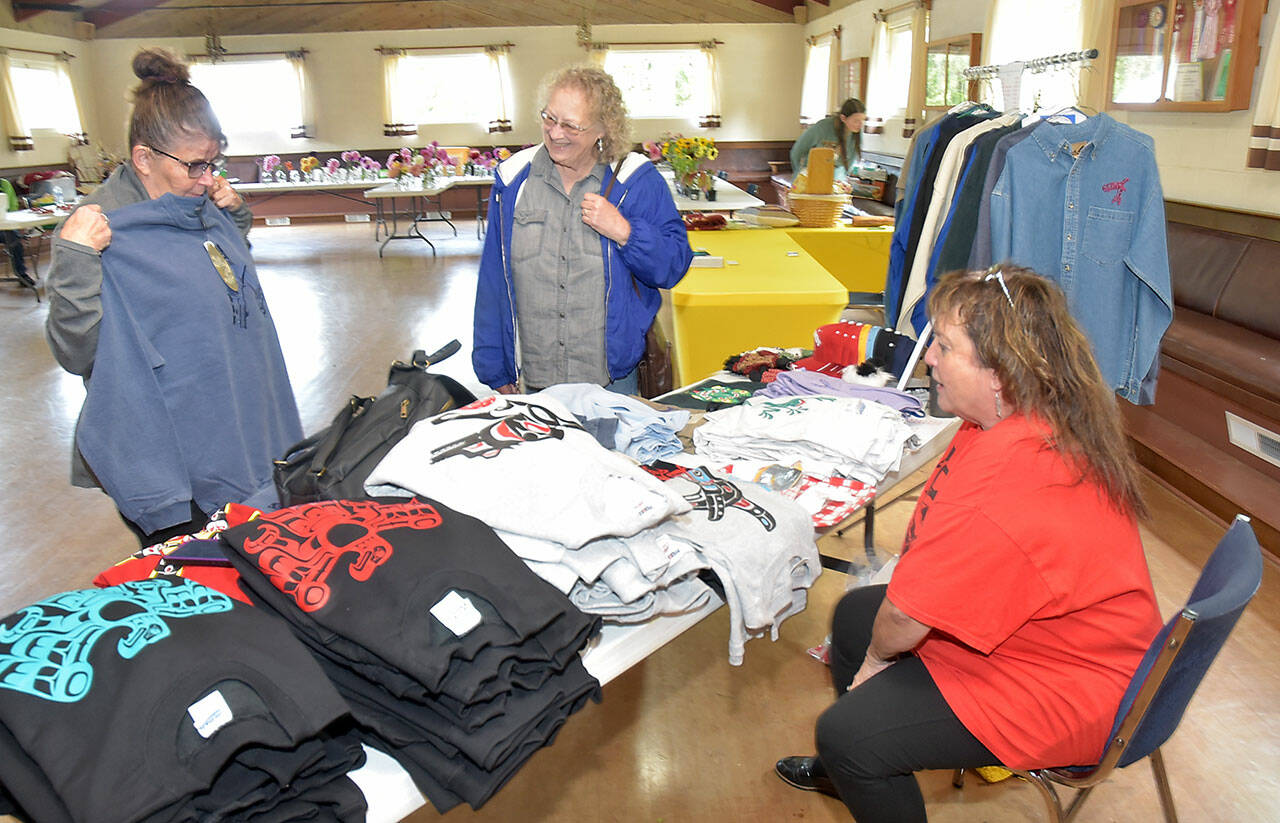 Jackie Leonard of Cottage Grove, Ore., left, examines a sweatshirt while Janet Estes of Joyce looks on at a merchandise table set up by Cindy Kelly at the Joyce Grange Hall on Saturday in Joyce. The venue was one location of the Great Strait Sale, a collection of garage and yard sales by residents along state Highway 112 from Port Angeles to Neah Bay. (Keith Thorpe/Peninsula Daily News)