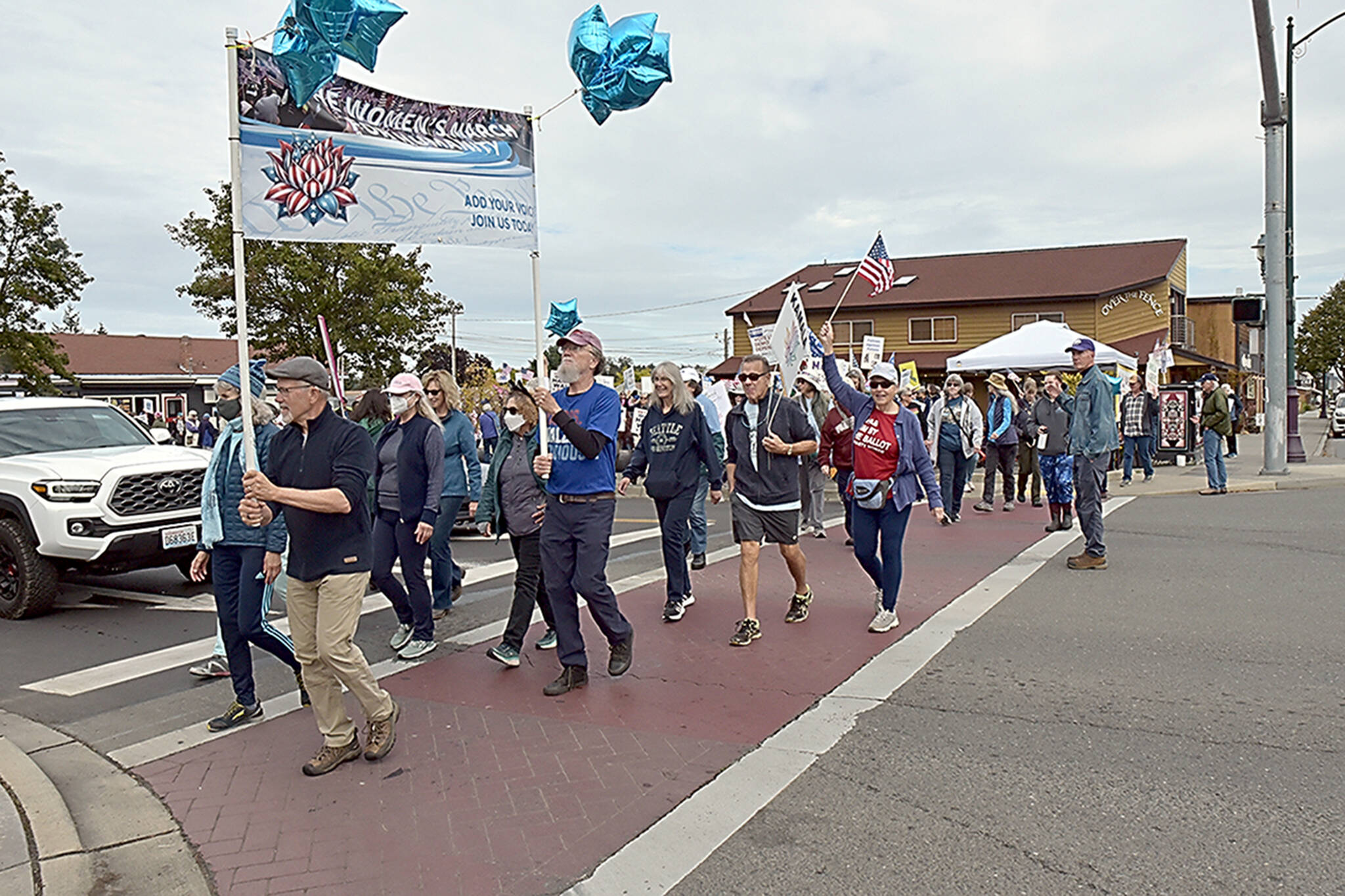 Participants in the Women’s March for Humanity cross Sequim Avenue at Washington Street in downtown Sequim on Saturday, part of a rally for U.S. presidential candidate Kamala Harris and running mate Tim Walz. The group of about 200 participants marched from Centennial Place Park to Fifth Avenue and back. (Keith Thorpe/Peninsula Daily News)