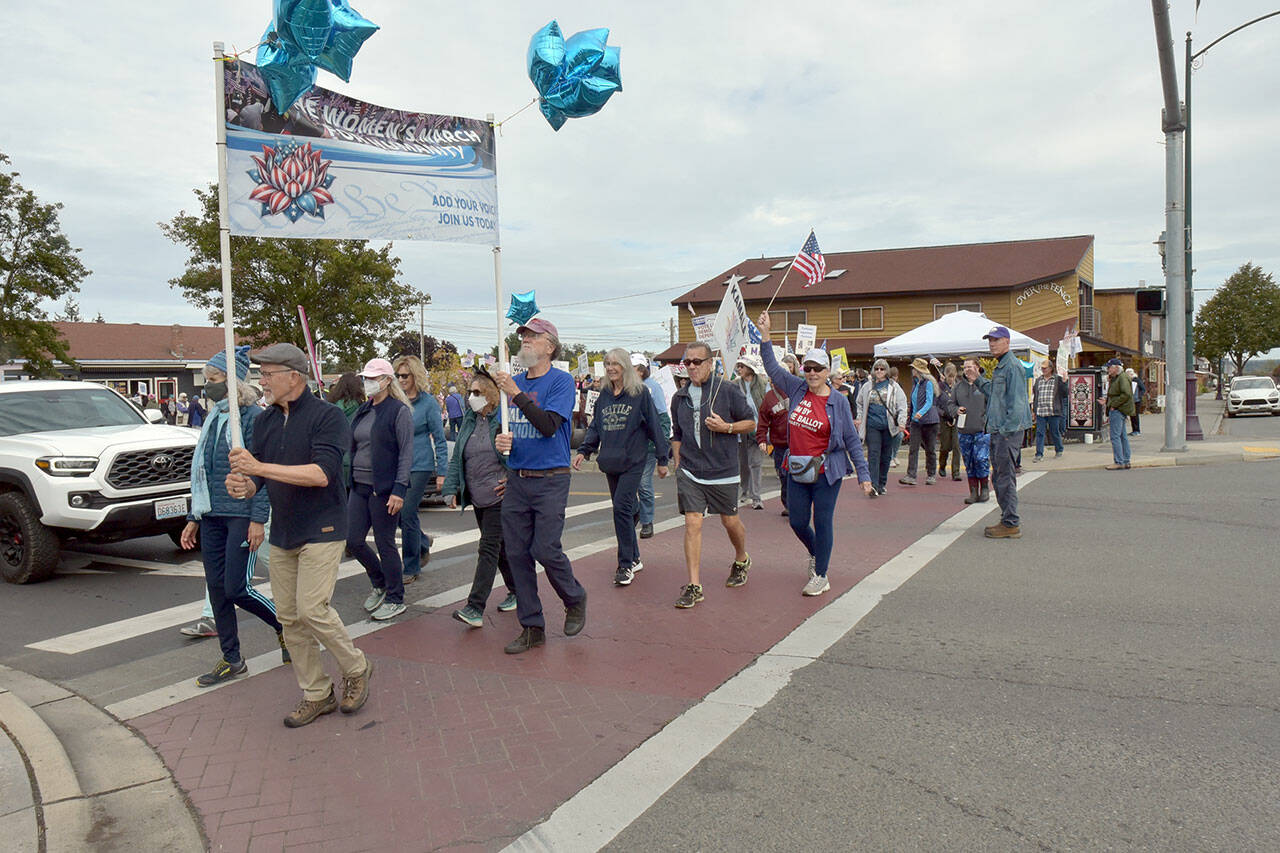 Participants in the Women’s March for Humanity cross Sequim Avenue at Washington Street in downtown Sequim on Saturday, part of a rally for U.S. presidential candidate Kamala Harris and running mate Tim Walz. The group of about 200 participants marched from Centennial Place Park to Fifth Avenue and back. (Keith Thorpe/Peninsula Daily News)