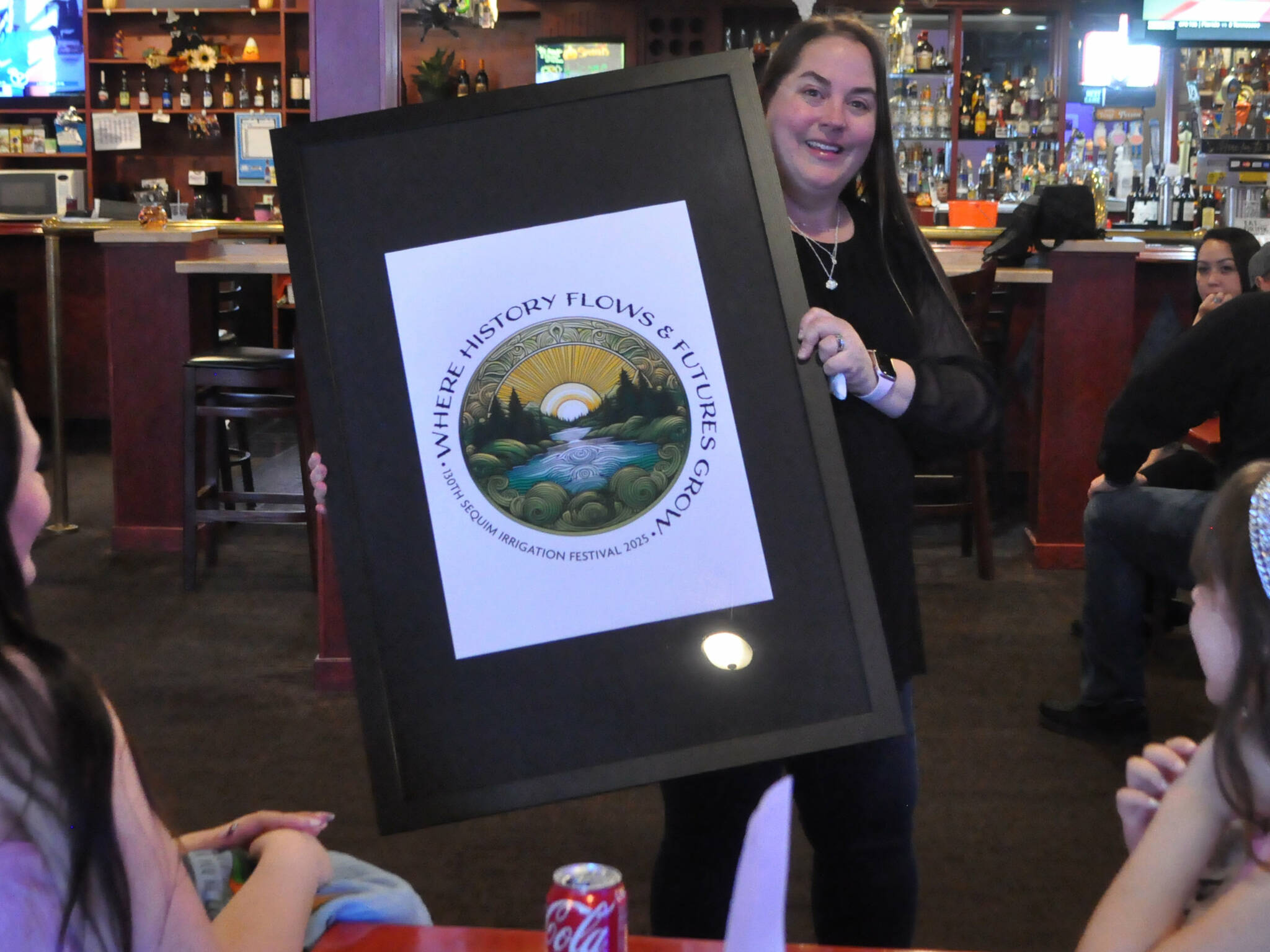 Michelle Rhodes, executive director of the Sequim Irrigation Festival, shows festival royalty the new logo and tagline “When History Flows and Futures Grow” for the 130th festival on Oct. 12 at the Oasis Bar and Grill. Sherry Scharschmidt designed the logo using artificial intelligence technology. (Matthew Nash/Olympic Peninsula News Group)