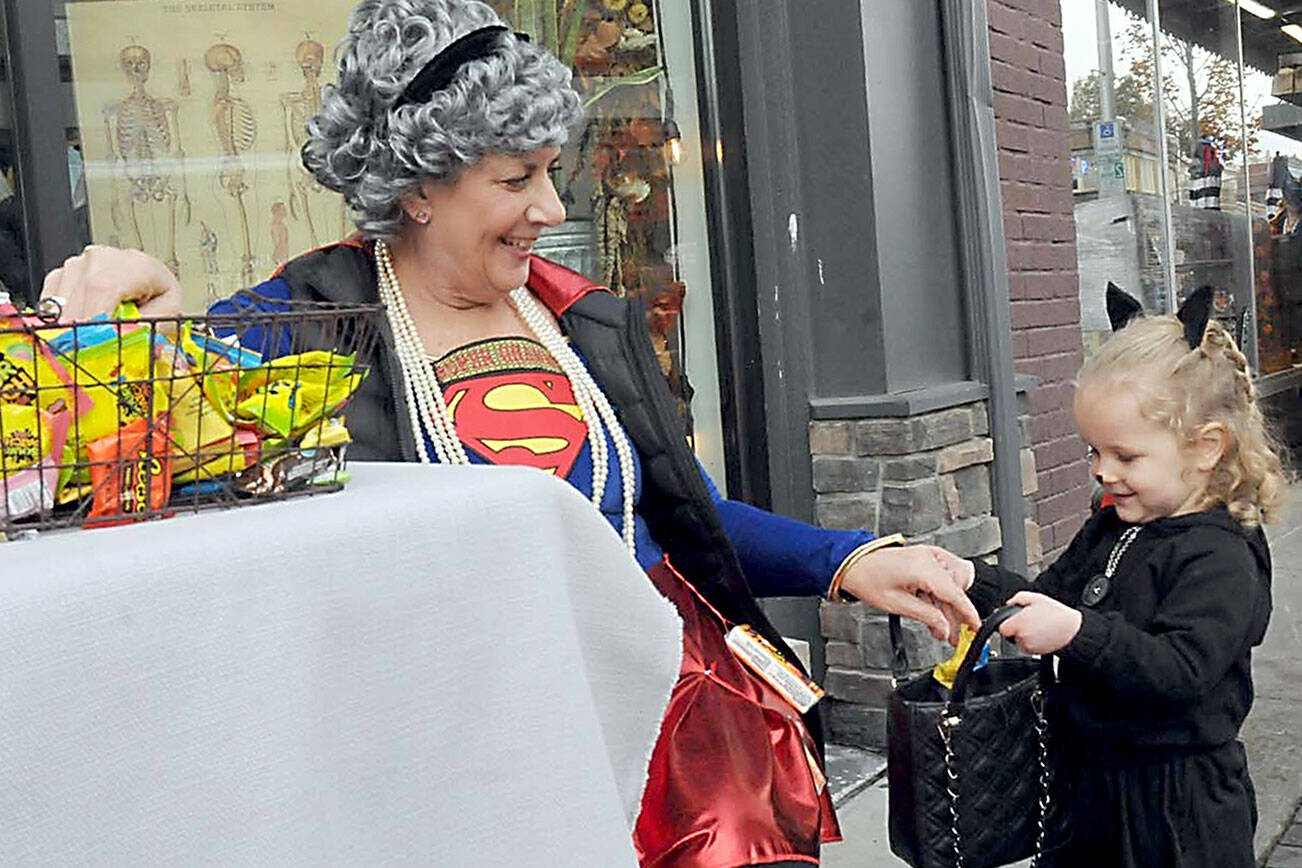 Ruby Speer, 3, of Port Angeles receives a treat from KaraLee Monroe of Kindred Collective as part of Thursday’s Halloween festivities in downtown Port Angeles. Hundreds of youngsters and adults made their way door-to-door in search of candy and other treasures. (Keith Thorpe/Peninsula Daily News)