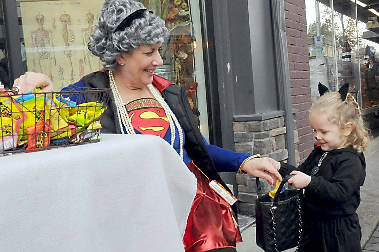 Ruby Speer, 3, of Port Angeles receives a treat from KaraLee Monroe of Kindred Collective as part of Thursday’s Halloween festivities in downtown Port Angeles. Hundreds of youngsters and adults made their way door-to-door in search of candy and other treasures. (Keith Thorpe/Peninsula Daily News)