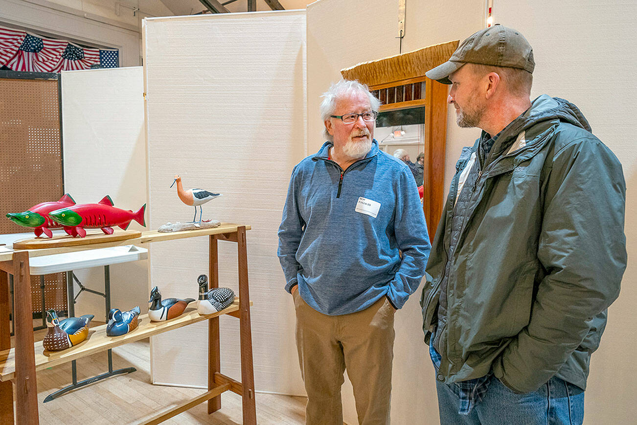 Decoy carver Ben Tyler, left, talks about the carvings he has on display to Brian Erickson, from Juneau, Alaska, during the Port Townsend Woodworkers Show at the Legion Hall in Port Townsend on Saturday. (Steve Mullensky/for Peninsula Daily News)