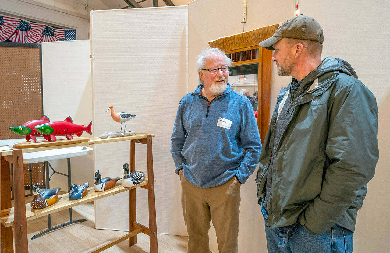 Decoy carver Ben Tyler, left, talks about the carvings he has on display to Brian Erickson, from Juneau, Alaska, during the Port Townsend Woodworkers Show at the Legion Hall in Port Townsend on Saturday. (Steve Mullensky/for Peninsula Daily News)