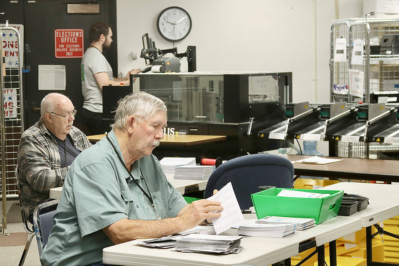 Ray Farrell, left, and Daniel Cain, center, prepare mail-in ballots for counting on Tuesday morning at the Clallam County courthouse in Port Angeles. The tabulating machine can be seen in the background with its operator. Election results, released after press time Tuesday, are online at www.peninsuladailynews.com. Full coverage will appear in Thursday’s print edition. (Dave Logan/for Peninsula Daily News)