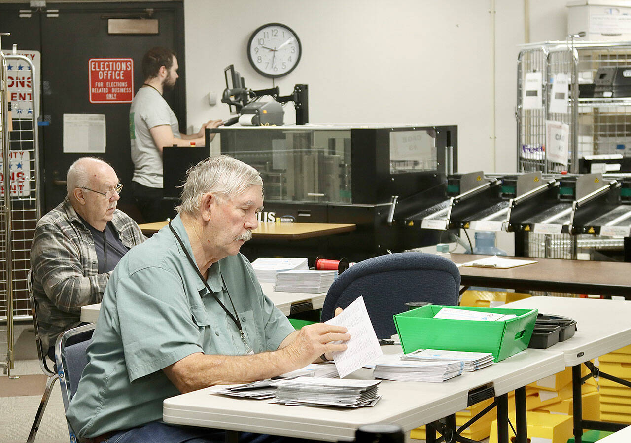 Ray Farrell, left, and Daniel Cain, center, prepare mail-in ballots for counting on Tuesday morning at the Clallam County courthouse in Port Angeles. The tabulating machine can be seen in the background with its operator. Election results, released after press time Tuesday, are online at www.peninsuladailynews.com. Full coverage will appear in Thursday’s print edition. (Dave Logan/for Peninsula Daily News)