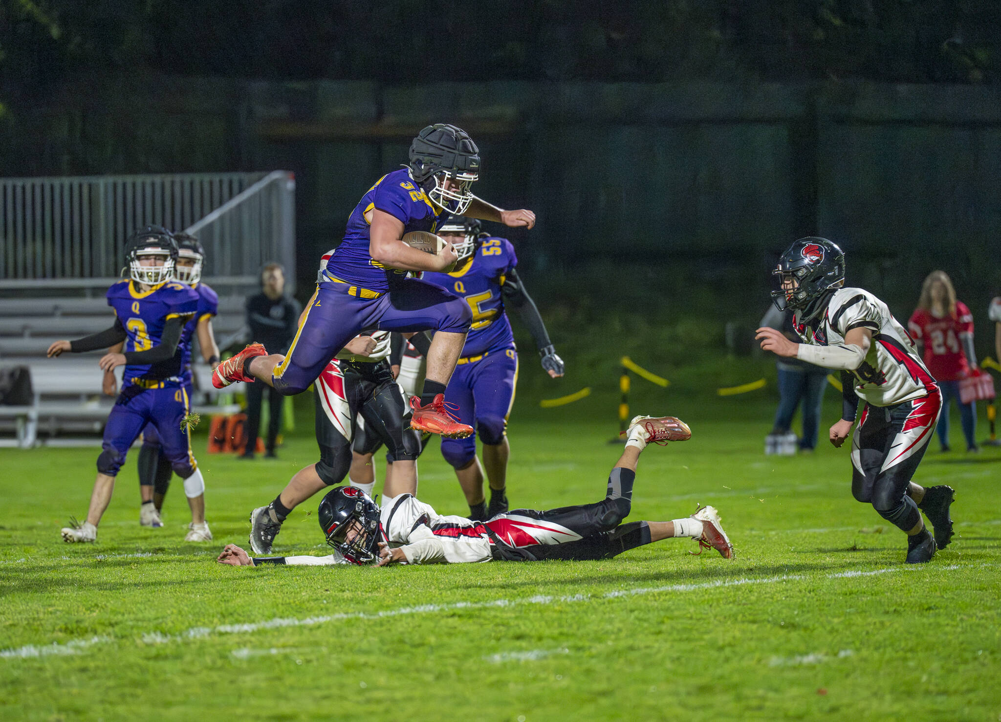 Steve Mullensky/for Peninsula Daily News Quilcene’s Mason Iverson leaps over his would-be Oakville Acorn tackler and runs for a first down in the first quarter of a Class 1B Quad District winner-to-state-game played under the lights on Friday in Port Townsend.