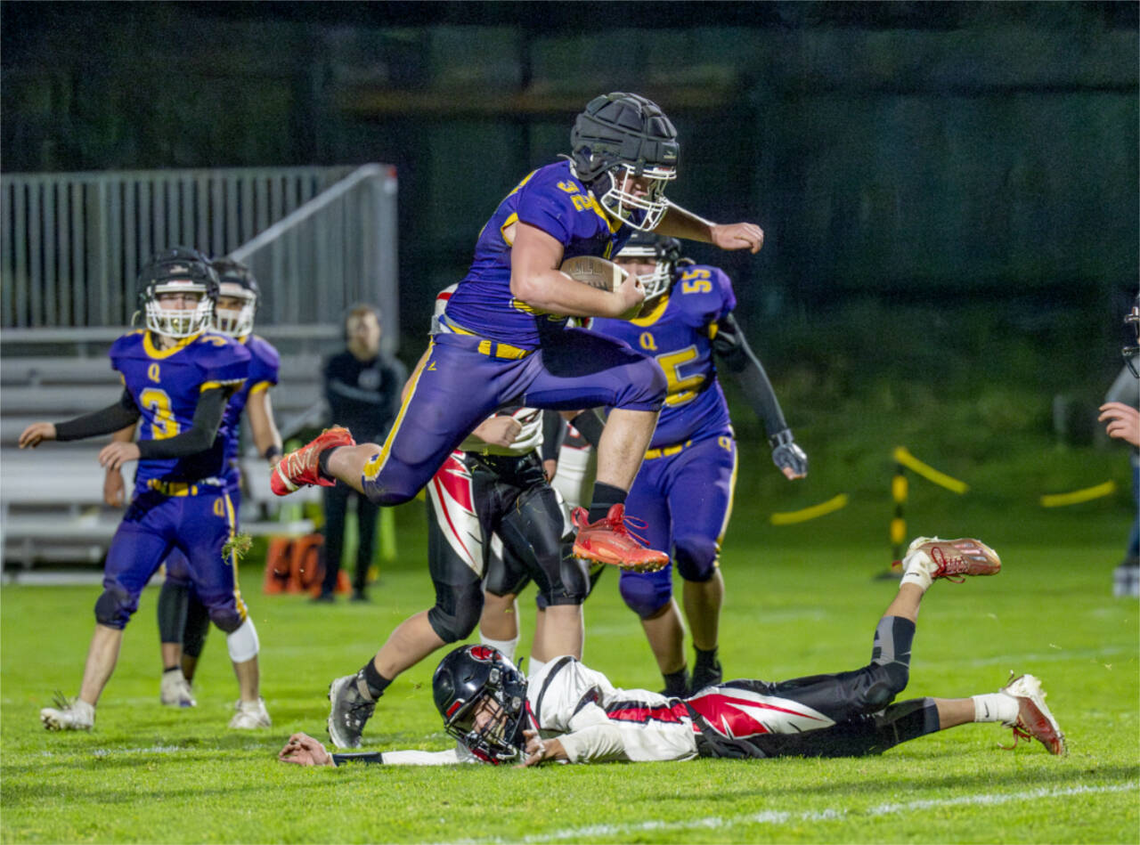 Steve Mullensky/for Peninsula Daily News
Quilcene's Mason Iverson leaps over his would-be Oakville Acorn tackler and runs for a first down in the first quarter of a Class 1B Quad District winner-to-state-game played under the lights on Friday in Port Townsend.