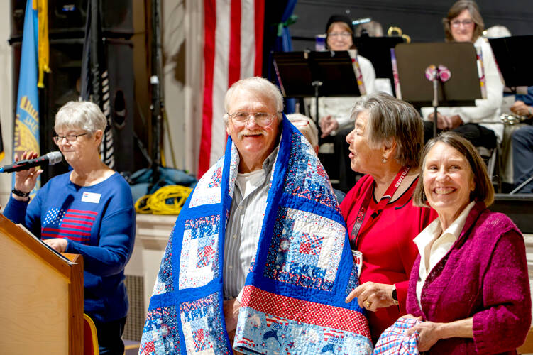 Former Marine Joseph Schwann of Port Townsend smiles as he receives a Quilt of Valor from Kathy Darrow, right, and another member of Quilts of Valor during the Veterans Day event at the American Legion Marvin G. Shields Memorial Post 26 in Port Townsend on Monday. Group leader Kathey Bates, left, was the emcee of the event. (Steve Mullensky/for Peninsula Daily News)