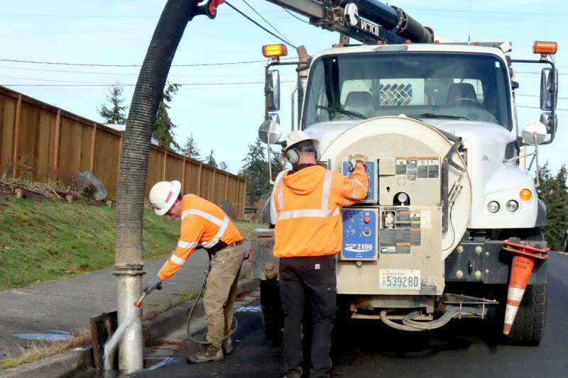 Greg Haskins, left, and Travis Truckenmiller of the city of Port Angeles perform annual cleaning of the city’s catch basins. They used a sprayer and additional tools to suck out all the debris, mostly leaves, to prevent flooding. (Dave Logan/for Peninsula Daily News)