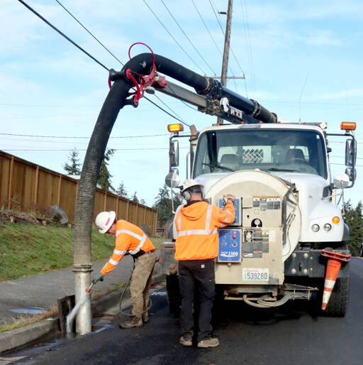 Greg Haskins, left, and Travis Truckenmiller of the city of Port Angeles perform annual cleaning of the city’s catch basins. They used a sprayer and additional tools to suck out all the debris, mostly leaves, to prevent flooding. (Dave Logan/for Peninsula Daily News)