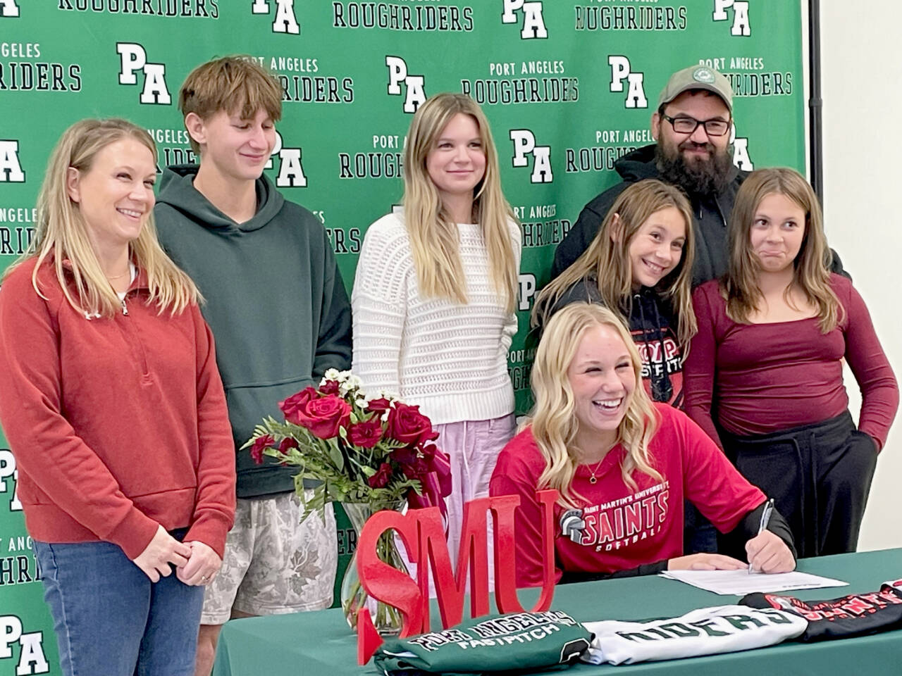 High School junior Heidi Leitz (at table) signs a letter of commitment on Friday with St. Martin's University to play softball surrounded by her family. From left are mother Stephanie Leitz; brother Owen Leitz, 16; sister Allison Leitz (13); sister Anna Leitz (11); father Ed Leitz; and sister Audrey Leitz (11). (Paula Hunt/Peninsula Daily News)