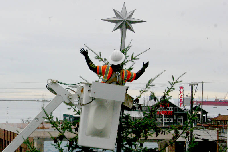 A Port Angeles city worker places a tree topper on the city’s Christmas tree, located at the Conrad Dyar Memorial Fountain at the intersection of Laurel and First streets. A holiday street party is scheduled to take place in downtown Port Angeles from noon to 7 p.m. Nov. 30 with the tree lighting scheduled for about 5 p.m. (Emma Maple/Peninsula Daily News)