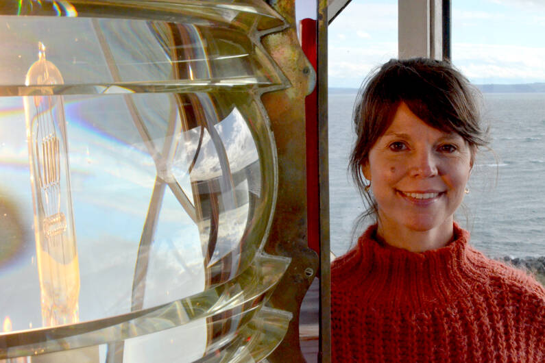 Lighthouse keeper Mel Carter next to the original 1879 Fresnel lens in the lamp room at the Point Wilson Lighthouse. (Elijah Sussman/Peninsula Daily News)