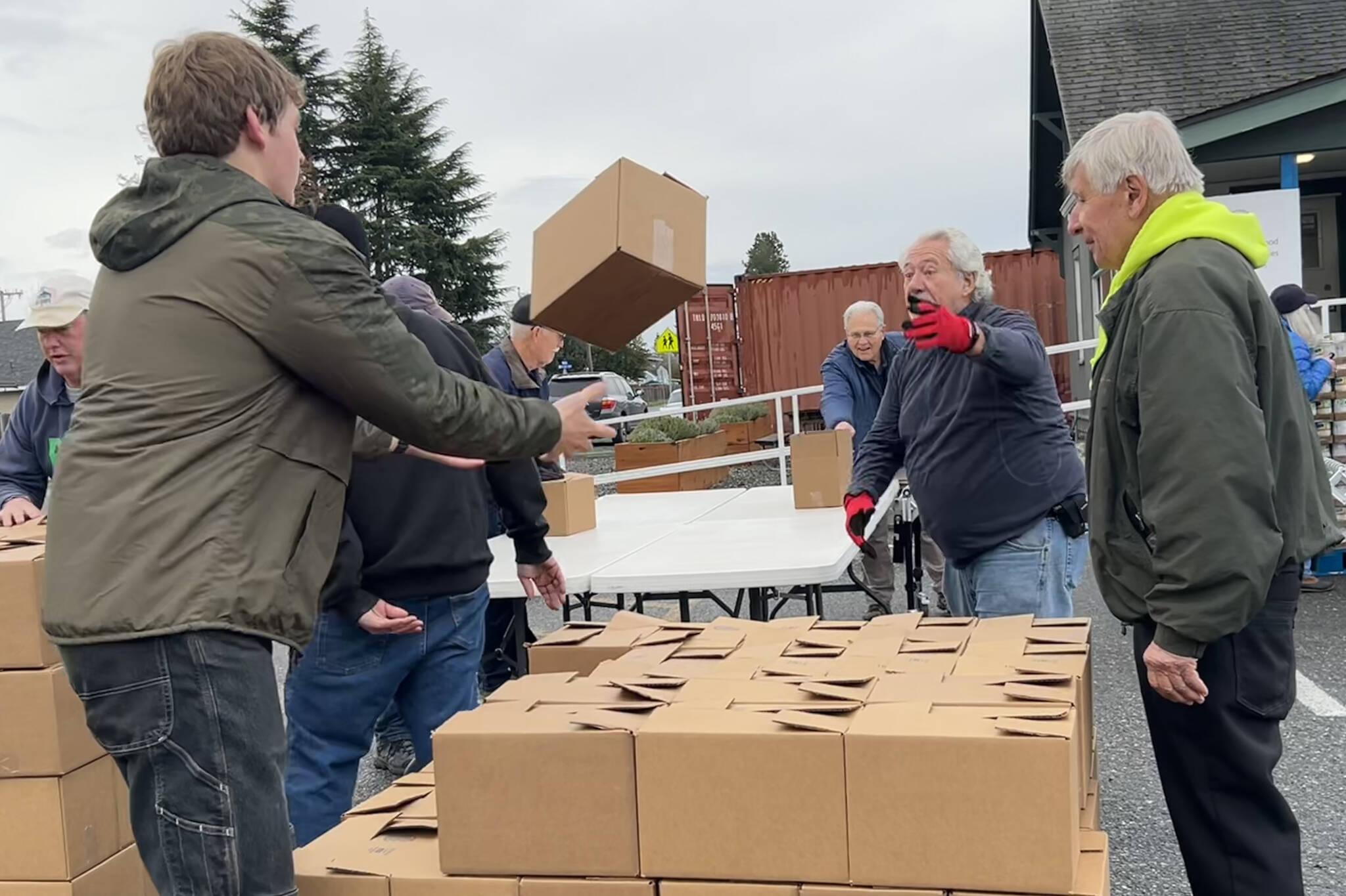 Harvey Hochstetter tosses a box of food to Cameron Needham to stack with fellow volunteers like Bill Needham, right, for the Sequim Food Bank’s Holiday Meal Bag Distribution event. Cameron, his father Ty and grandfather Bill were three generations helping the program. (Matthew Nash/Olympic Peninsula News Group)