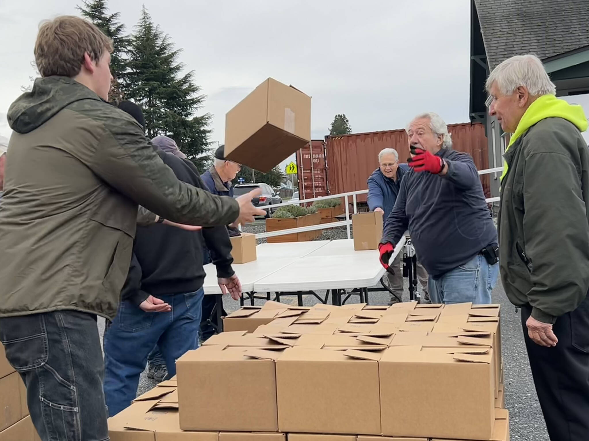 Harvey Hochstetter tosses a box of food to Cameron Needham to stack with fellow volunteers like Bill Needham, right, for the Sequim Food Bank’s Holiday Meal Bag Distribution event. Cameron, his father Ty and grandfather Bill were three generations helping the program. (Matthew Nash/Olympic Peninsula News Group)