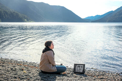 Paranormal investigator Amanda Paulson sits next to a photo of Hallie Illingworth at Lake Crescent, where Illingworth’s soap-like body was discovered in 1940. Paulson stars in a newly released documentary, “The Lady of the Lake,” that explores the history of Illingworth’s death and the possible paranormal presence that has remained since. (Ryan Grulich)