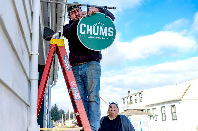 Connor Cunningham of Port Townsend, an employee of the Port of Port Townsend, hangs a sign for new business owner Lori Hanemann of Port Townsend on Friday at her shop in what was a former mortgage office at Point Hudson Marina. (Steve Mullensky/for Peninsula Daily News)