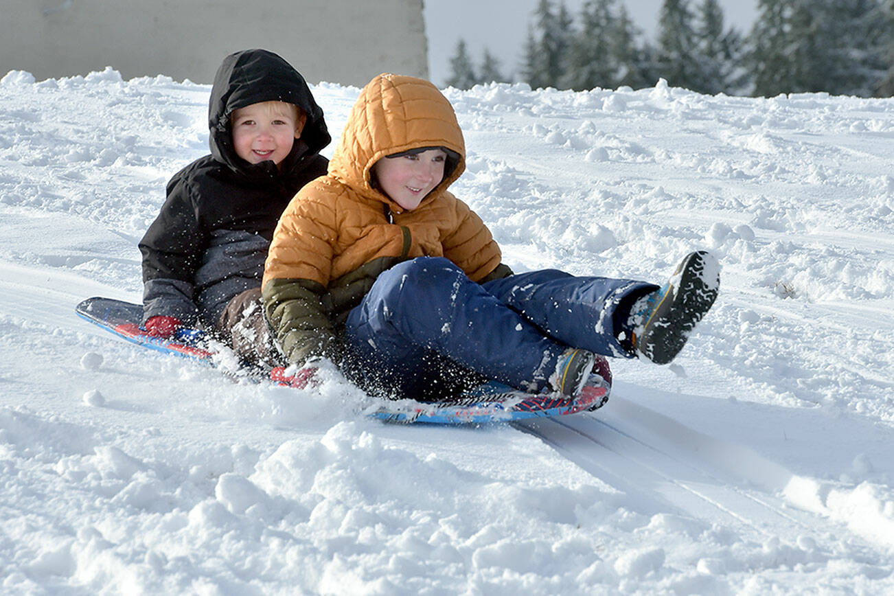 Port Angeles brothers Finley Bornsworth, 3, left, and Oliver Bornsworth, 6, take a snowy sled ride on the campus of Port Angeles High School on Tuesday. Overnight snowfall left a mantle of white over much of the North Olympic Peninsula with an additional chance of snow showers forecast through the weekend. (Keith Thorpe/Peninsula Daily News)