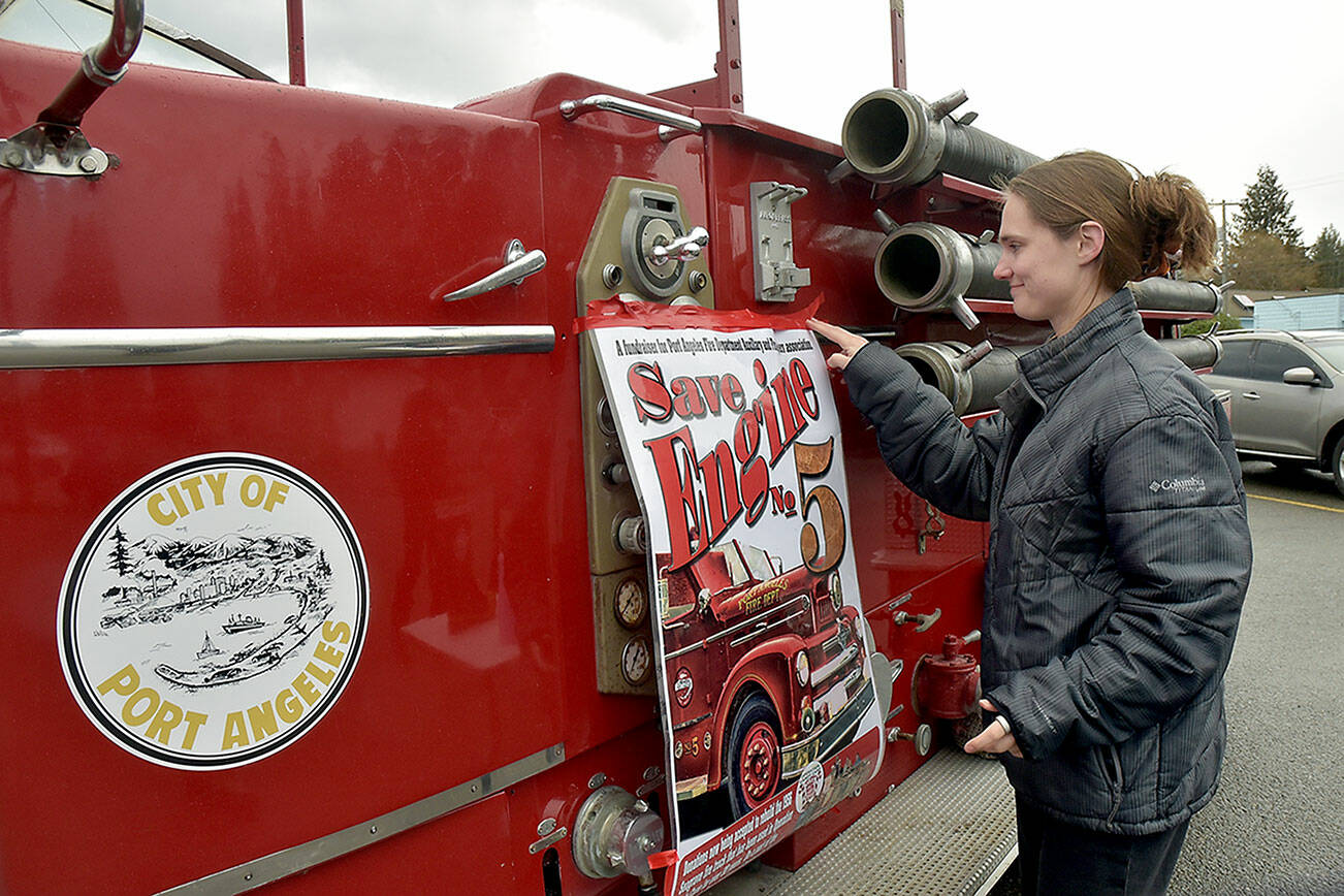 Samantha Herik, an EMT with the Port Angeles Fire Department, attaches a poster to the side of her department’s vintage 1956 Seagrave fire truck during a fundraising drive on Saturday in the Swain’s General Store parking lot in Port Angeles. PAFD is collecting donations to rebuild the retired vehicle, known as “No. 5,” with a restored engine and transmission. The truck is used primarily for the annual Operation Candy Cane food bank fundraising drive, along with other promotional purposes. (Keith Thorpe/Peninsula Daily News)