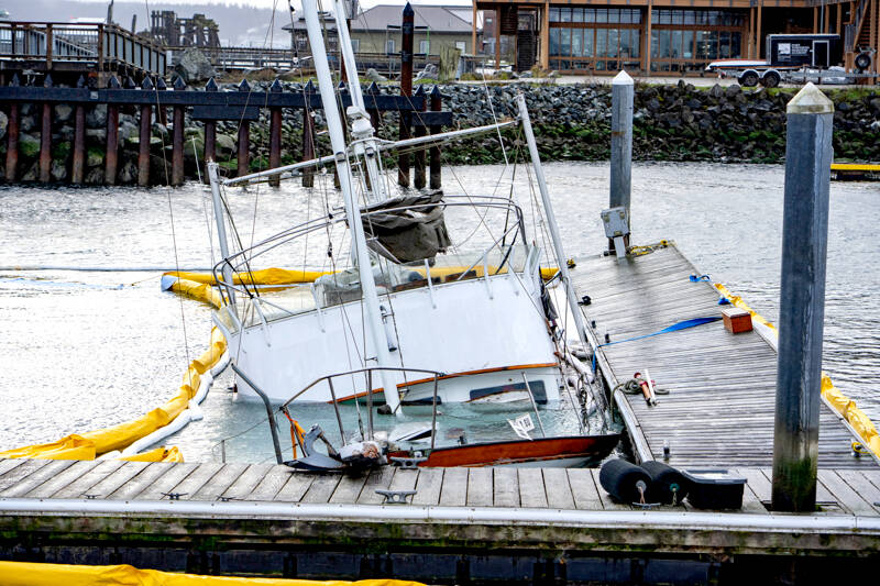 A yellow oil-containment boom surrounds the 60-foot power cruiser Goldfinch after it sank at the Point Hudson Marina on Saturday. The boat was on its way from Seattle to Anacortes when it started taking on water. It made it to the Point Hudson and struck the breakwater as it entered the harbor but was able to be steered into slip 3, where it immediately sank. Port of Port Townsend staff responded and deployed the hard boom and absorbent material to contain the fuel spill. As of Monday afternoon, about 1,000 gallons of diesel had been recovered by Global Diving and Salvage with 650 gallons from the fuel tanks of the Goldfinch and the remainder being sopped up by absorbent material. The U.S. Coast Guard and the state Department of Ecology responded and performed additional containment. A plan for recovery was in the works, but it wasn’t expected to begin before Wednesday due to weather. (Steve Mullensky/for Peninsula Daily News)