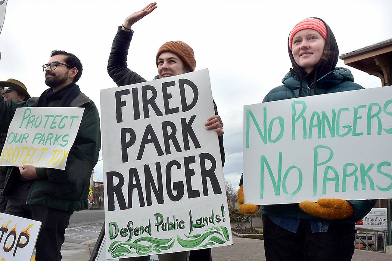 Hazel Galloway, a recently laid-off science communications specialist with the National Park Service, center, is flanked by Andy Marquez, a marine science student assisting Olympic National Park, left, and Mari Johnson, a supervisor with ONP partner Washington Conservation Corps during a protest at The Gateway in Port Angeles against the Trump administration’s downsizing of the NPS workforce. (Keith Thorpe/Peninsula Daily News)