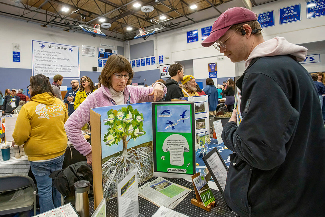 Cindy Taylor of Port Townsend, representing the environmental group Local 20/20, points to printed information available about the organization to an interested party while at the Jefferson County Connectivity Summit at Chimacum High School on Saturday. (Steve Mullensky/for Peninsula Daily News)